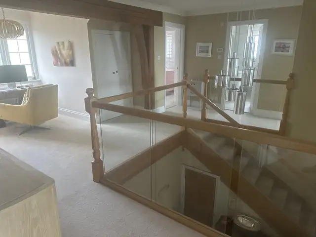 Neutral painted landing and open plan room above a glass and oak balustrade